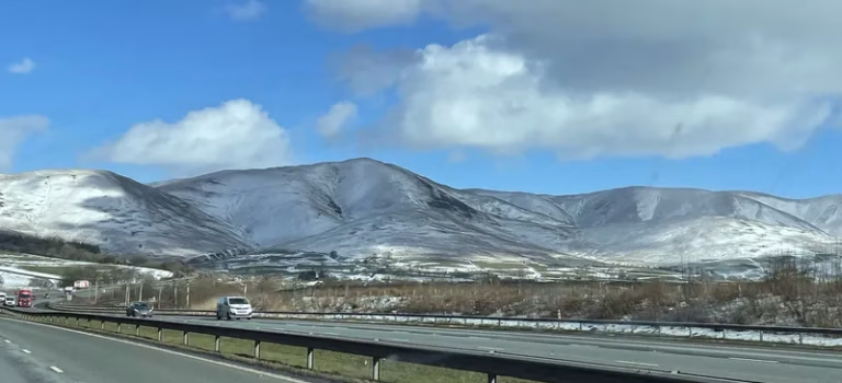 Places to Stop on Your Journey to Serenity 22 Barend Scenic view of snow-capped mountains and hills under a blue sky from the M6 motorway heading northbound towards Scotland.