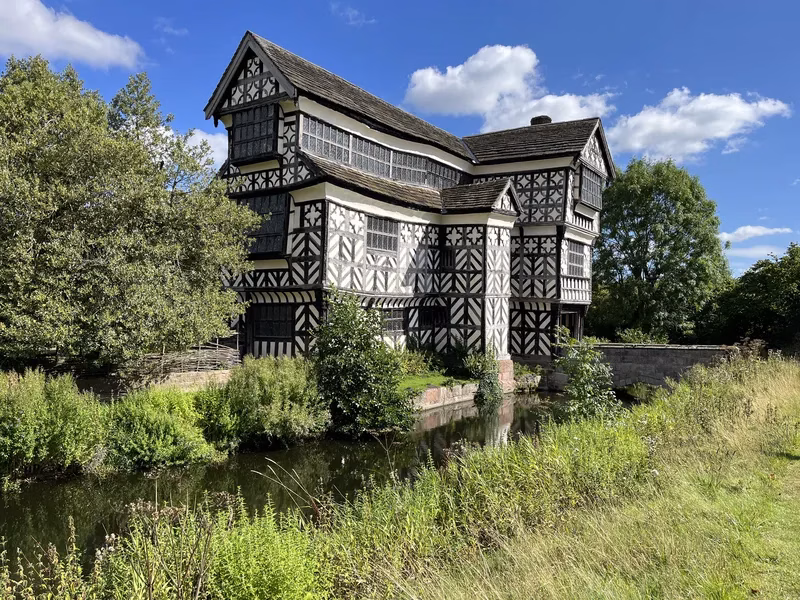 The historic black and white timber-framed Tudor manor house of Rufford Old Hall next to a calm canal on a sunny day.