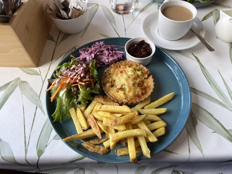 A homemade red onion quiche served with fries, mixed green salad, coleslaw, and a small pot of dark chutney relish at Caddie's Cove Bistro near Colvend.